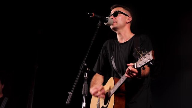 A rock music player is performing onstage at rock festival, close-up. The artist is playing guitar and singing. High quality 4k footage