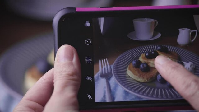 To Take a pic with smartphone on blueberry pancakes in a plate. Traditional food for breakfast or brunch. Homemade fluffy pancakes, cup of coffee, spoon and fork on table. food photography 