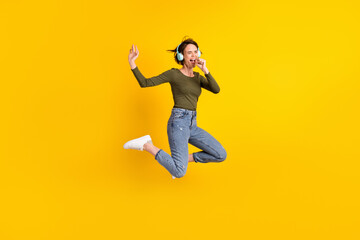 Fototapeta na wymiar Full length photo of crazy girl jump sing song use hand as mic wear wireless headset isolated on bright yellow color background