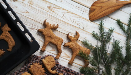 Homemade sweet Christmas cookies in the shape of animals with fir branches are laid out on a wooden background. New year is table decoration.