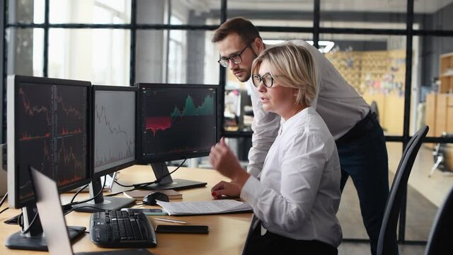 Woman shows results to man that goes angry by negative results and walks away. Male and female stockbrokers in formal clothes works in the office with financial market and graphs on monitors.