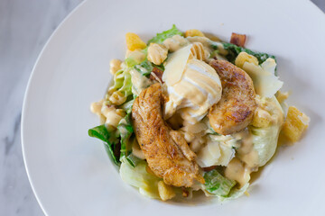 Caesar salad with fresh green vegetable is mixed with grilled chicken, boiled white egg and crispy bread. It’s a healthy food concept.