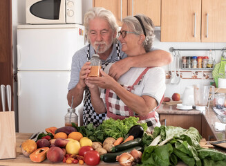 Cheerful senior couple enjoying a fresh smoothie homemade with fruit and vegetables for a healthy lifestyle. Assortment of raw fresh ingredients on the table
