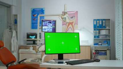 Computer with green screen placed in front of camera in empty modern equipped stomatological room. Stomatology clinic with nobody in it prepared for next patient with mock-up, chroma key pc display