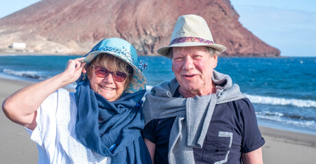 Portrait of two happy senior people enjoying winter holidays by the sea, smiling and looking at camera. Active carefree retired couple enjoying their retirement