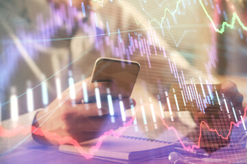 Double exposure of man's hands holding and using a phone and financial graph drawing. Analysis concept.