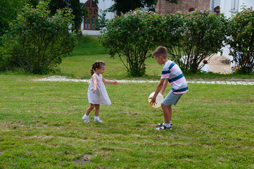 Very cute children, a boy and a girl, brother and sister play with the ball in the park on the lawn on a summer day