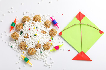 indian festival makar sankranti concept : sesame seed ball or til ke laddo and tilgul in bowl and colorful paper kite on white background