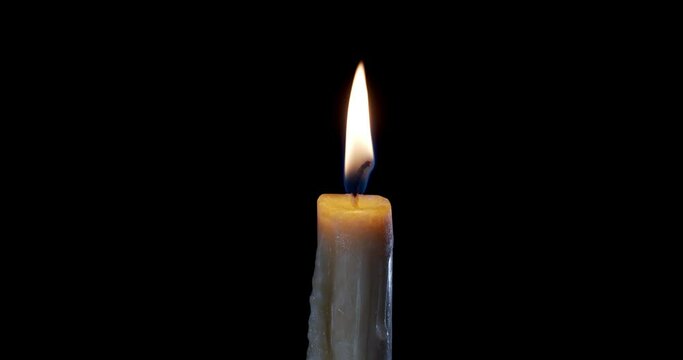 A single white candle burning. Isolated candle burning with dark background. White paraffin candle with yellow shades burns on a black background. Perfect for the layer with different blending modes.