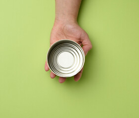 open metal round tin can in a female hand on a green background