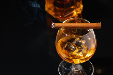 Burning cigar and glass of whisky on black background