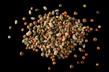 Mixed legumes and cereals, peeled barley, green, yellow and dark red lentils, half green peas, black white beans, green beans isolated on black background, top view