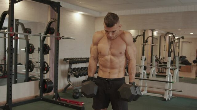 Young strong man training in the gym and doing exercises dumbbells shrugs for pumping the shoulders and trapezius muscle