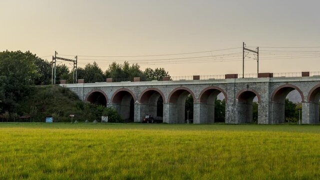Timelapse of a railway viaduct with passing trains and cars in an underpass during a sunny day with moving clouds in the sky.