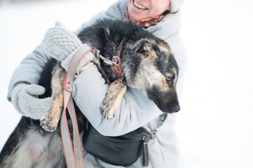Smiling woman holding mongrel dog in winter forest. Close up