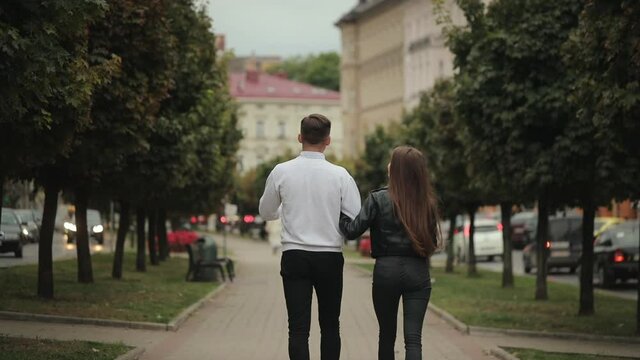 A man and a woman are walking in the park. They are talking and holding hands. Shooting from behind. 4K.