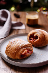Puff pastry rolls with fruit and coffee on wooden table against Christmas tree. Danish pastries. Christmas breakfast