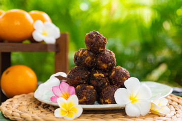 sweet balls of dried fruit decorated with tropical frangipani flowers in thailand on koh samui island, oranges in the background with plumeria flowers, vegan and vegetarian sweets