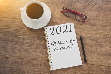 Close up planner with the inscription 2021, what to expect, coffee cup, glasses, pen, on a brown wooden table