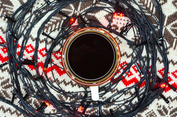 New Year's atmosphere, mood and coziness, warming winter drink black coffee, and christmas lights on a knitted sweater lifestyle at home
