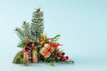 Beautiful composition of Christmas decoration on light blue background with fir branches, red berries and gift boxes. Minimal creative concept.