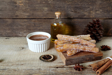 homemade Spanish caramel churros in the wooden slat on the wooden table together with chocolate...