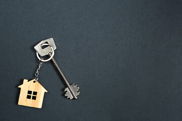Key chain in the shape of wooden house with key on a black background. Building, design, project,...