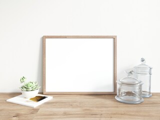 Blank horizontally oriented rectangular picture frame with thin wooden border standing on wooden surface. Glass utensil and flower on side. 3D Illustration.