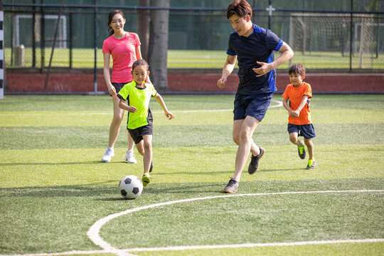 Happy young family playing football on soccer field