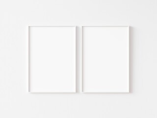 Two blank vertically oriented rectangular picture frames with thin white border hanging on white wall. 3D illustration.