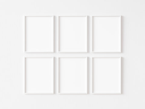 Six blank vertically oriented rectangular picture frames with thin white border hanging in two rows on white wall. 3D illustration.