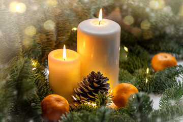 Christmas decoration with lighted candles, ripe tangerines and fir branches on blurred garland light background