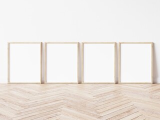 Four blank vertically oriented rectangular picture frames with light wood border standing on wooden floor leaning on white wall. 3D Illustration.