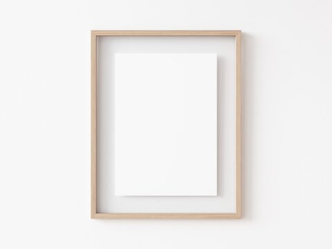 Blank vertically oriented rectangular light wood picture frame hanging on white wall. 3D Illustration.