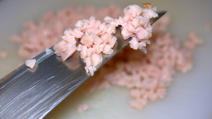 Finely chopped pieces of ham on a sharp knife, meat minced by knife