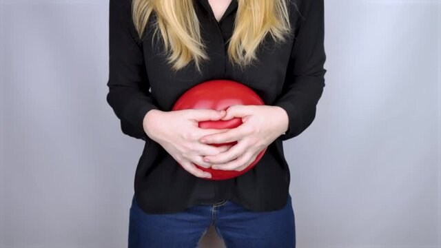 Bloating and flatulence concept. The woman holds a red balloon near the abdomen, which symbolizes bloating. Intestinal tract and digestive system. Problems with flatulence and gastrointestinal tract