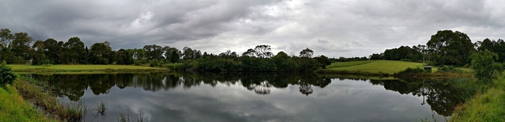 Beautiful panoramic morning view of a pond with reflections of trees and dark clouds on water, Fagan park, Galston, Sydney, New South Wales, Australia
