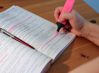 A female hand holding highlighter pen. In her workbook, she underlines important issues with a pink highlighter.