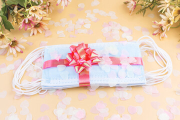 Medical protective masks with pink bow, flower and confetti isolated on pastel background. Flat lay. Gift for holiday, birthday, Mother's Day, Valentine's day, Women's Day during coronavirus pandemic.