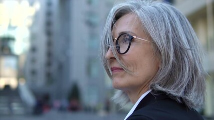 Close up mature woman with gray hair standing outdoor, enjoying wind on her face