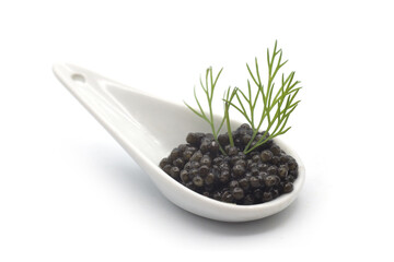 Closeup of caviar in a white ceramic spoon with a dill leaf on white background