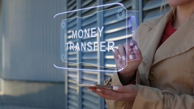 Unrecognizable businesswoman interacts HUD hologram with text Money Transfer. Woman in the coat uses the technology of the future mobile screen on the background of the city
