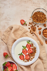 Greek yogurt in white bowl with ingredients for making breakfast granola and fresh strawberries on old beige table. Top view.