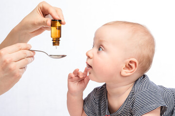 Mother feeding baby boy with vitamin or liquid medicine using spoon