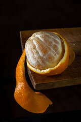 Orange on a wooden surface. Citrus fruit. Orange half peeled. Orange peel hanging down