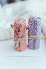 Close up of two natural decorative  beewax candles with dried flowers and a honey aroma for interior and tradition on a white table. A delicate color palette. Handmade