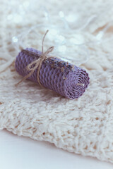 Fototapeta na wymiar Close up of lavender natural decorative beewax candle with dried flowers and a honey aroma for interior and tradition on a white knitted sweater. A delicate color palette. Handmade