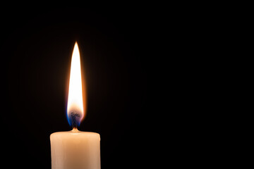 Burning candle in front of a black background with place for text.