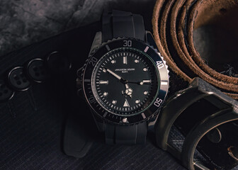 Image of a men's watch a leather belt on top of a gray waist coat and jacket