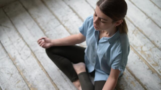 Young woman meditating sitting on the floor in an empty construction apartment, top view
